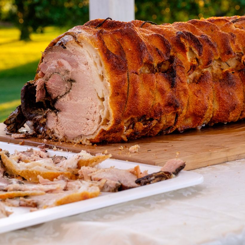 Porchetta arrosto affettata su un tagliere di legno durante un servizio catering